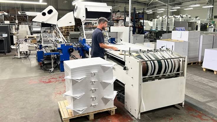 A staff member operating a folding machine, with folded signatures stacked ready alongside it